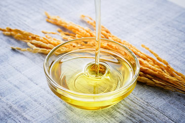 Rice bran oil being poured into a glass bowl with rice grains